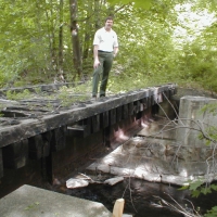 CRT bridge_oblique010514 Some improvements take major steps. In 2001, Cochituate State Park Supervisor Carey VandenAkker demonstrates the deteriorated deck of one of two railroad bridges just north of Old Connecticut Path. Creosoted timbers and crossties are heavy, and don't mix well with the trout in Cochituate Brook.